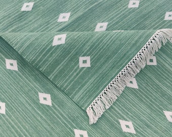 May include: A green rug with a white diamond pattern and white fringe. The rug has a textured surface.