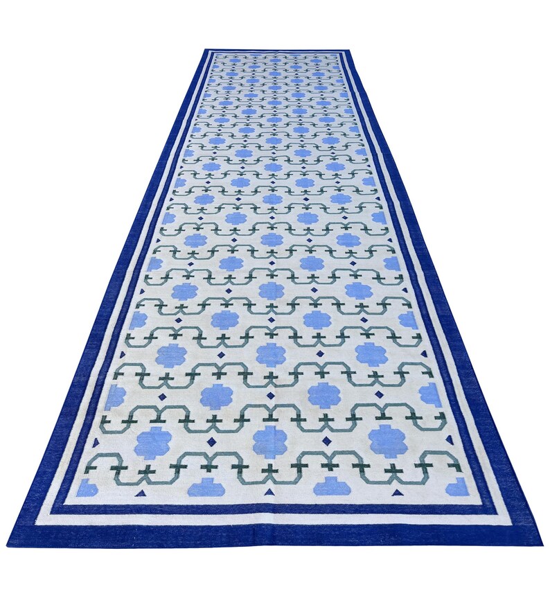 May include: A long white runner rug with a blue and green geometric pattern. The rug has a blue border.