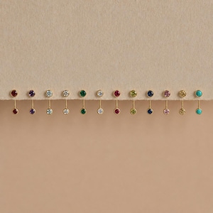Puede incluir: Una colección de doce pendientes tipo barra en tono dorado, cada uno con dos piedras preciosas redondas engastadas en bisel de varios colores, incluyendo rojo, morado, azul claro, blanco, verde, amarillo, azul oscuro, rosa y turquesa.