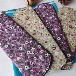 May include: Four reusable cloth pads with floral patterns in shades of green, purple, and white. The pads are arranged in a fan shape and are sitting on a blue fabric pouch.