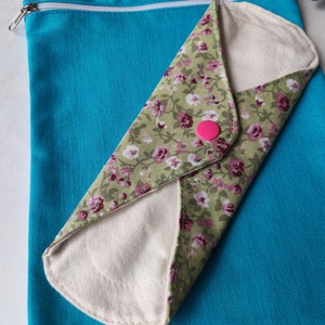 May include: A reusable cloth menstrual pad with a floral print, folded and placed inside a turquoise zippered pouch.