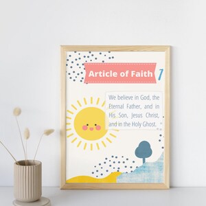 May include: A framed print with a colorful illustration of a sun, a tree, and a yellow and blue landscape. The text "Article of Faith 7" is in a pink banner at the top. The text below reads "We believe in God, the Eternal Father, and in His Son, Jesus Christ, and in the Holy Ghost."