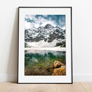 May include: A framed photograph of a mountain lake with snow-capped peaks reflecting in the clear, green water.  The lake is surrounded by rocky mountains and a few trees.