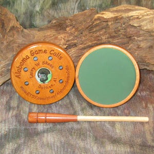 May include: A wooden turkey call with a green felt bottom and a wooden striker. The call is engraved with the text "Alabama Game Calls, Larry W Skeen, Dothan, Al, www.etsy.com/shop/AlabamaGameCalls".