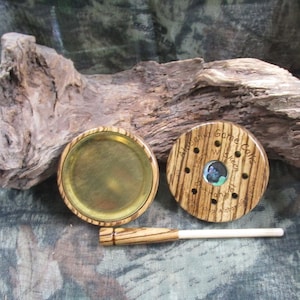 May include: A wooden turkey call with a brass bottom and a wooden striker. The call is engraved with the words "Alabama Game Calls" and "Lusty McKeen Turkey Talker".