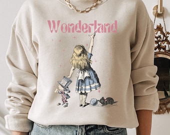 May include: A beige sweatshirt with a graphic print of Alice in Wonderland. The text "Wonderland" is printed in pink on the front of the sweatshirt.