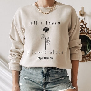 May include: A beige sweatshirt with a black rose and the text "all I loved I loved alone Edgar Allan Poe" printed on the front.