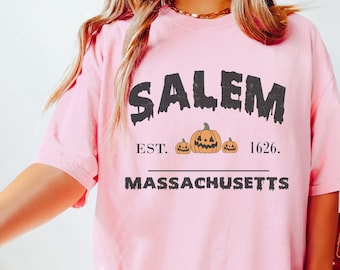 Könnte beinhalten: Rosa T-Shirt mit einer schwarzen Grafik, auf der "Salem Est. 1626. Massachusetts" mit drei orangefarbenen Kürbissen steht.