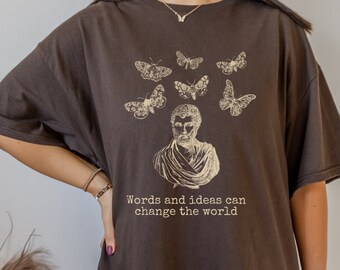 May include: A brown oversized t-shirt with a graphic of a man's bust with butterflies around his head. The text "Words and ideas can change the world" is printed below the graphic.