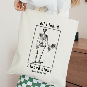 Peut inclure: Sac fourre-tout blanc avec une illustration noir et blanc d'un squelette tenant une rose. Le texte "all I loved I loved alone Edgar Allan Poe" est imprim&eacute; sur le sac.