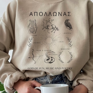 以下が含まれることがあります： ギリシャ神アポロンをモチーフにしたベージュのトレーナー。トレーナーには、アポロンの属性を表すシンボルがプリントされています。シンボルには、リュート、月桂樹の冠、弓矢、カラス、太陽などがあります。トレーナーには、「ΑΠΟΛΛΩΝΑΣ」と「GOD OF SUN, MUSIC AND POETRY」の文字もプリントされています。