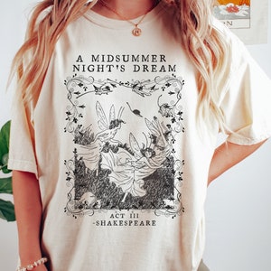 May include: A white t-shirt with a black and white illustration of fairies from Shakespeare's A Midsummer Night's Dream. The text "A Midsummer Night's Dream", "Act III", and "Shakespeare" is printed on the shirt.