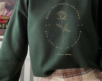 May include: A dark green sweatshirt with a gold graphic of a rose and the quote "Never love anyone who treats you like you're ordinary." by Oscar Wilde.
