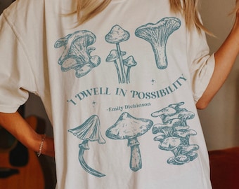 May include: A white t-shirt with a blue mushroom graphic and the text "I dwell in possibility - Emily Dickinson".