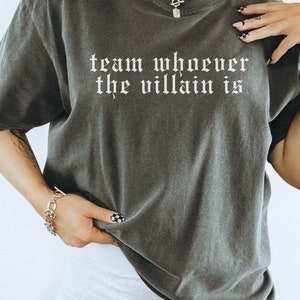 May include: A dark gray t-shirt with the text "team whoever the villain is" printed in white on the front.