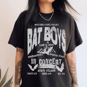 K&ouml;nnte beinhalten: Schwarzes T-Shirt mit einem wei&szlig;en Grafikdruck einer Band namens "Bat Boys" im Konzert. Die Grafik enth&auml;lt den Bandnamen, "Lord of Night", "Shadowsinger", "Warrior-Heart" und das Datum "Oct. 4th".