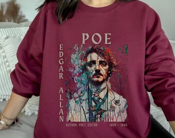 Puede incluir: Sudadera color burdeos con un estampado gráfico de Edgar Allan Poe. El estampado presenta un retrato estilizado de Poe con elementos abstractos coloridos. El texto "POE" está por encima del retrato, y "EDGAR ALLAN" está a la izquierda del retrato. El texto "AUTHOR, POET, EDITOR 1809-1849" está debajo del retrato.