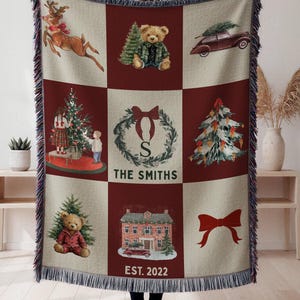 Könnte beinhalten: Eine gewebte Weihnachtsdecke mit einem Rastermuster. Die Quadrate zeigen festliche Bilder wie ein Rentier, einen Teddybären, einen Weihnachtsbaum und ein Haus. Das mittlere Quadrat zeigt einen Kranz mit "THE SMITHS" und "EST. 2022".