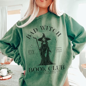 Könnte beinhalten: Grünes Sweatshirt mit einer schwarzen Grafik einer Hexe mit dem Text "Bad Witch Est 1974 Book Club What Happens in Book Club Stays in Book Club"