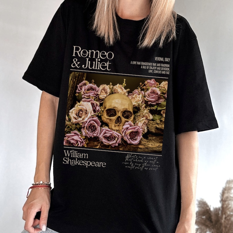 May include: Black t-shirt with a graphic print of a skull surrounded by pink roses. The text "Romeo & Juliet" is printed above the graphic and "William Shakespeare" is printed below. The text "VERONA, ITALY" is printed in the upper right corner of the graphic. The text "A love that transcends time and tradition. A tale of tragedy and devotion. Love, conflict and fate." is printed below the text "VERONA, ITALY".