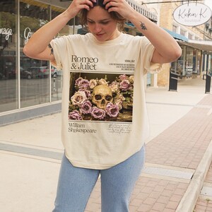 May include: A beige t-shirt with a graphic print of a skull surrounded by pink roses. The graphic also includes the text "Romeo & Juliet", "William Shakespeare", and a quote from the play.
