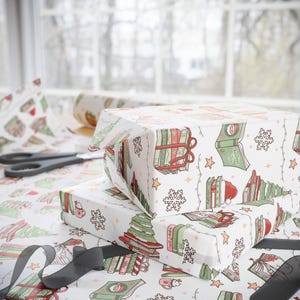 May include: Two wrapped gifts with white wrapping paper featuring a festive pattern of books, Christmas trees, snowflakes, and stars. A pair of scissors and a roll of matching wrapping paper are visible in the background. A black ribbon is in the foreground.