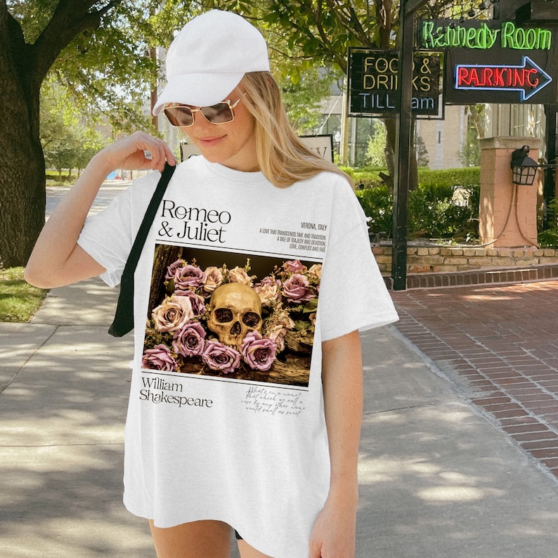 May include: White t-shirt with a graphic print of a skull surrounded by pink roses. The text "Romeo & Juliet" and "William Shakespeare" are printed on the shirt.