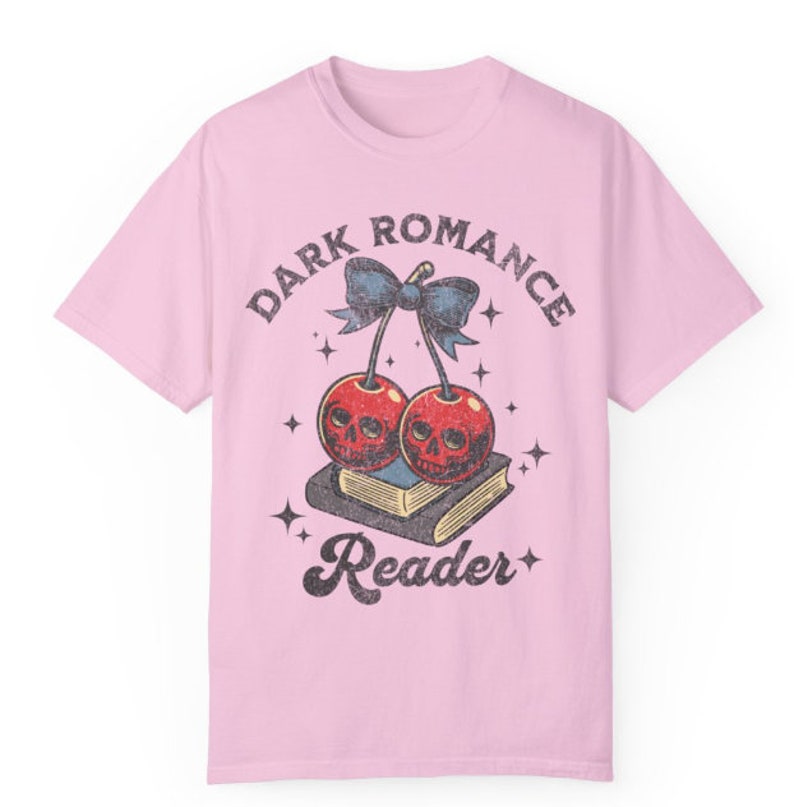 K&ouml;nnte beinhalten: Hellrosa T-Shirt mit einem Grafikdesign. Das Design zeigt zwei Kirschen mit Totenkopfgesichtern, eine blaue Schleife und die Worte "DARK ROMANCE Reader" in einem Vintage-Stil. Die Kirschen liegen auf einem Buch.