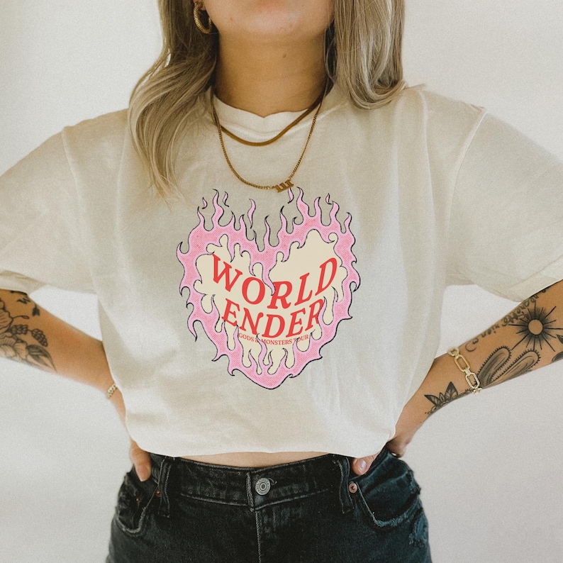 May include: A white t-shirt with a pink and yellow heart-shaped flame graphic. The text "WORLD ENDER" is written in red inside the heart. The text "YOUR MONSTERS YOUR TRUTH" is written in smaller red letters below the heart.