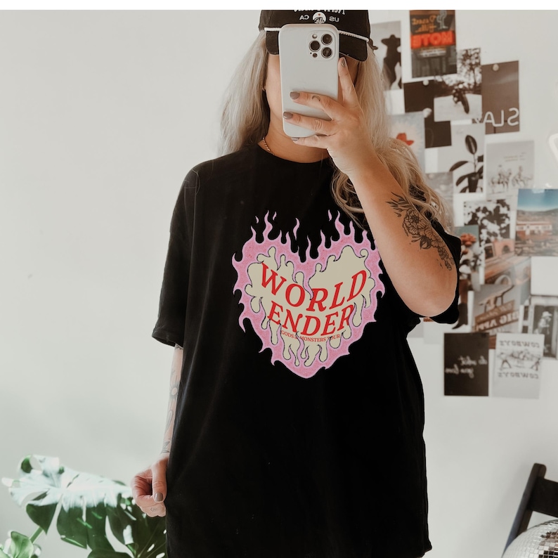 May include: Black oversized t-shirt with a pink and yellow heart graphic. The heart graphic has flames around it and the text "WORLD ENDER" inside.