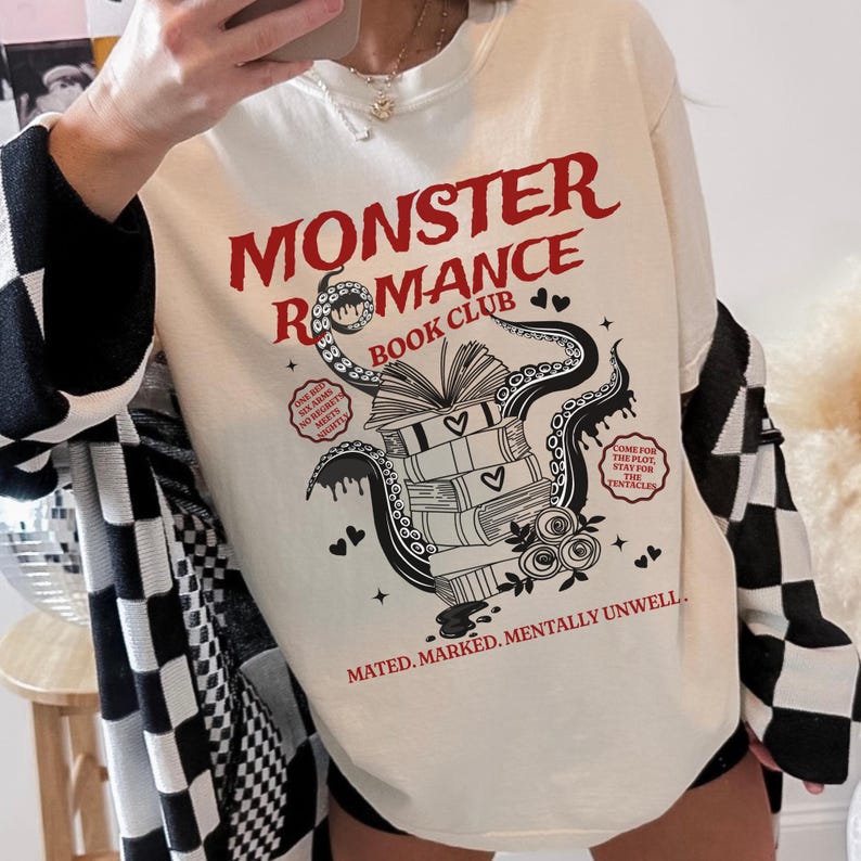Pu&ograve; includere: Felpa color crema con la scritta "MONSTER ROMANCE BOOK CLUB" in rosso. La grafica presenta un libro aperto sopra una pila di libri, con tentacoli, cuori e le frasi "ONE BED, SIX ARMS, NO REGRET, MEET NIGHT" e "COME FOR THE PLOT, STAY FOR THE TENTACLES".