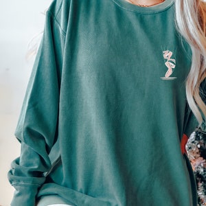 May include: A teal green long-sleeved sweatshirt with a pink ballerina graphic on the front.