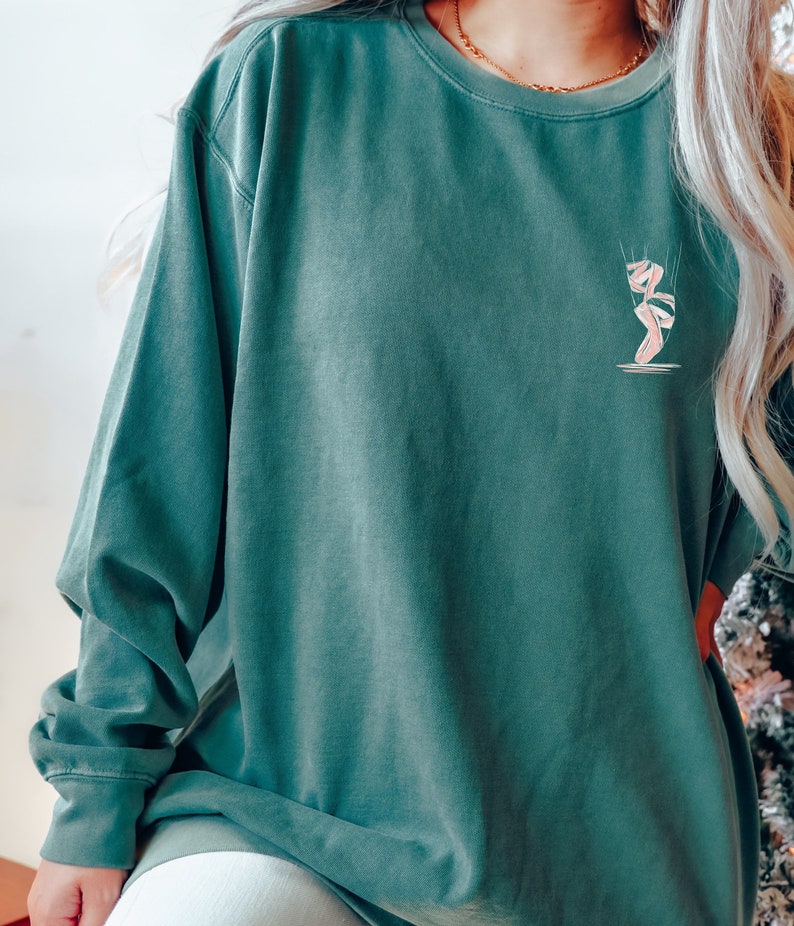 May include: A teal green long-sleeved sweatshirt with a pink ballerina graphic on the front.