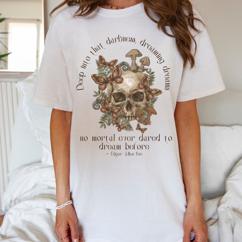 May include: White t-shirt featuring a skull surrounded by butterflies and mushrooms. The text "Deep into that darkness, dreaming dreams no mortal ever dared to dream before - Edgar Allan Poe" is printed on the shirt.