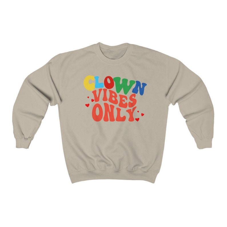 Może przedstawiać: Jasnobeżowa bluza z napisem "CLOWN VIBES ONLY" w kolorowych, retro literach. Tekst jest w tęczy kolor&oacute;w, z czerwonymi sercami otaczającymi tekst.