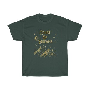 May include: A dark green t-shirt featuring a gold graphic of mountains, a crescent moon, and stars. The text "COURT OF DREAMS" is printed in gold on the shirt.