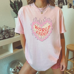May include: Pink t-shirt with a graphic of a heart on fire with the text "WORLD ENDER" inside the heart.
