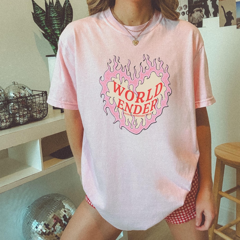 May include: Pink t-shirt with a graphic of a heart on fire with the text "WORLD ENDER" inside the heart.