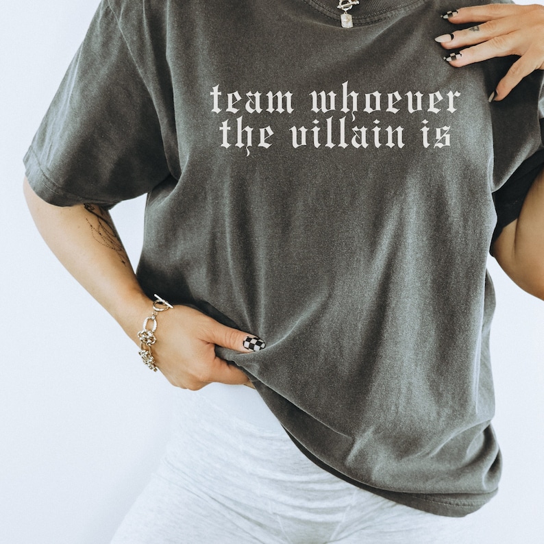 May include: A dark gray t-shirt with the text "team whoever the villain is" printed in white on the front.