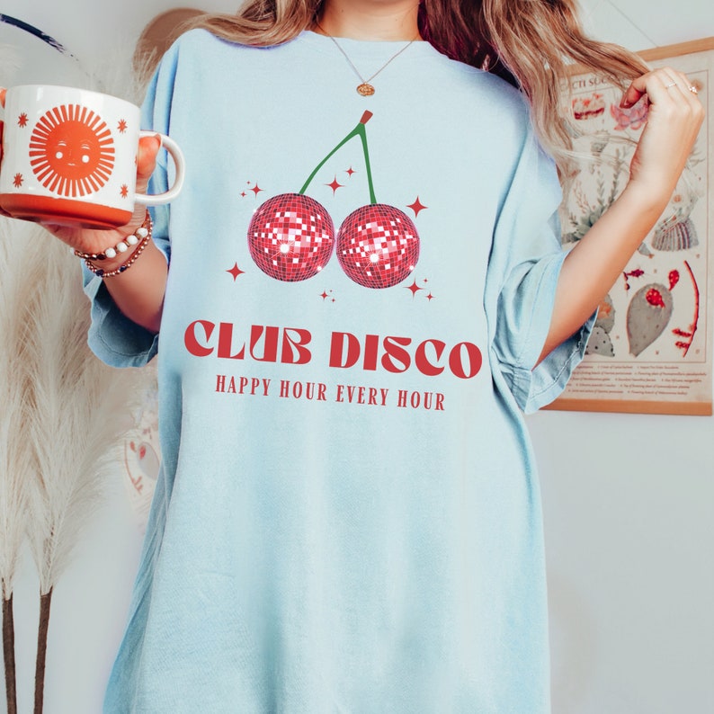 May include: Light blue t-shirt with a red cherry graphic. The cherry is made of disco balls. The text "Club Disco" and "Happy Hour Every Hour" is printed in red.