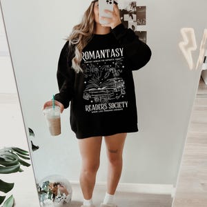 May include: Black sweatshirt with a white graphic design featuring a book, a dragon, and the text "Romantasy: Fantasy Worlds for Romantic Souls" and "Readers Society: Where Love Conquers Kingdoms".