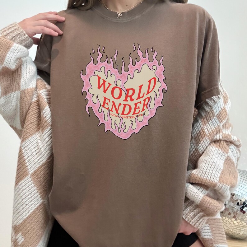 May include: A brown t-shirt with a pink and red graphic of a heart with flames. The text "WORLD ENDER" is inside the heart. The text "GODS & MONSTERS YOUTH" is below the heart.