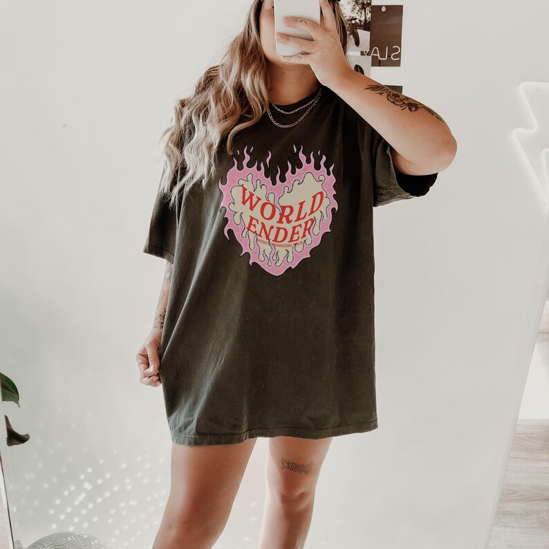 May include: A dark green oversized t-shirt with a pink and yellow heart graphic that says "WORLD ENDER" in red letters.