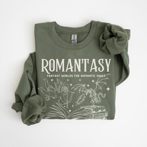 May include: A green sweatshirt with the text "ROMANTASY" and the words "Fantasy Worlds for Romantic Souls". The sweatshirt features a graphic of a winged cherub with a bow and arrow, a dragon, and a stack of books.