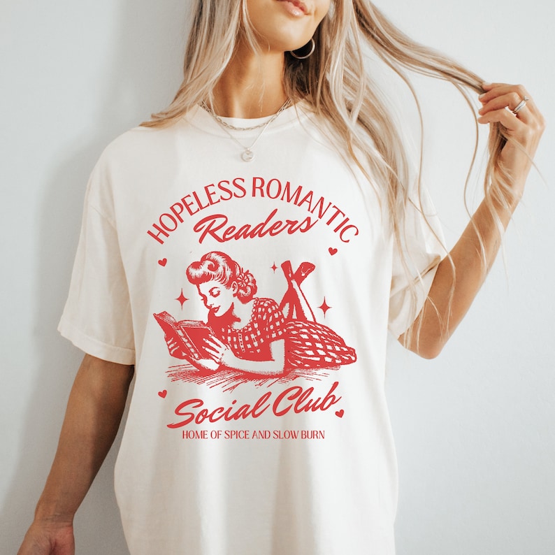 Peut inclure: T-shirt blanc avec un motif rouge d'une femme lisant un livre. Le motif dit "Hopeless Romantic Readers Social Club, Home of Spice and Slow Burn."
