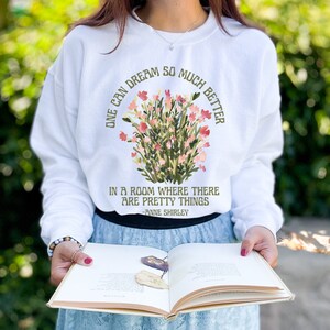 May include: White sweatshirt with a floral design and the text "One can dream so much better in a room where there are pretty things -Anne Shirley"