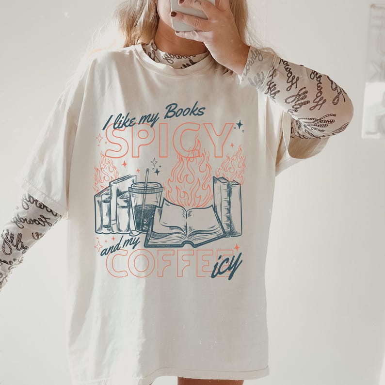 May include: Cream-colored oversized t-shirt with the text "I like my Books SPICY and my COFFEE icy" in teal and coral. The graphic includes books, a coffee cup, and flames. The shirt has long sleeves underneath.