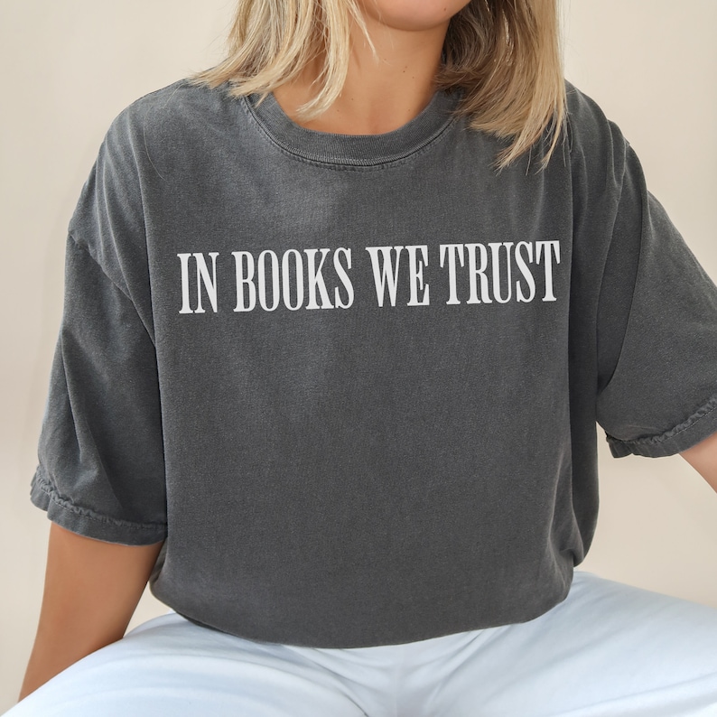 May include: A dark gray t-shirt with the text "IN BOOKS WE TRUST" printed in white on the front.