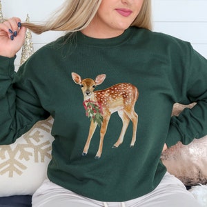 May include: A green sweatshirt with a watercolor illustration of a fawn wearing a red bow and holding a sprig of holly.