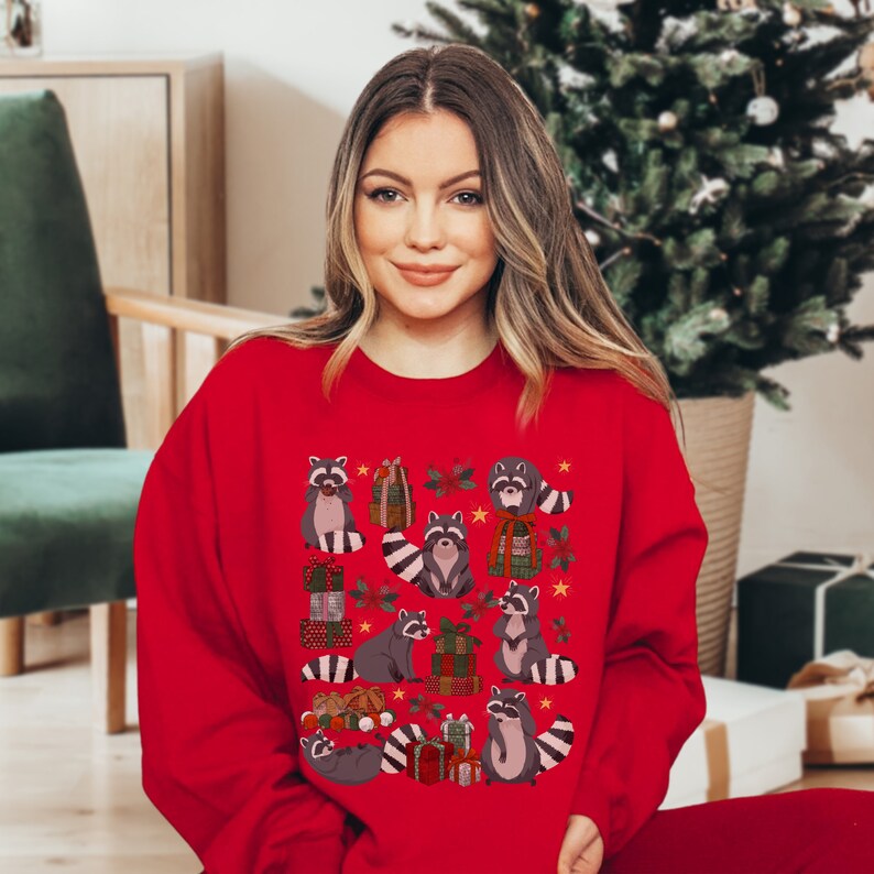 K&ouml;nnte beinhalten: Roter Weihnachtspullover mit einem Muster aus Waschb&auml;ren, die Geschenke halten und von Sternen und Blumen umgeben sind.